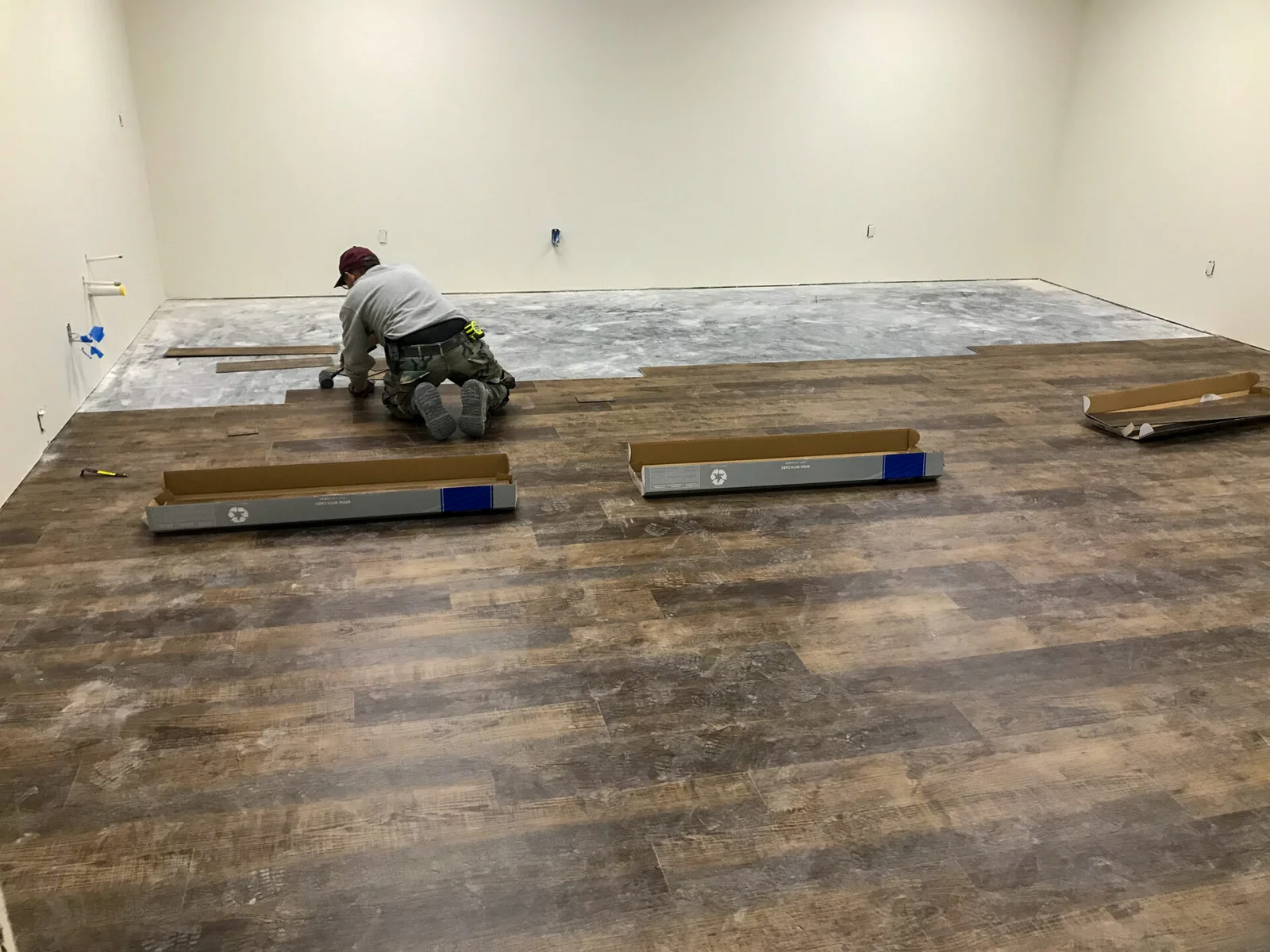 A worker installs laminate flooring in an empty room with unfinished walls.