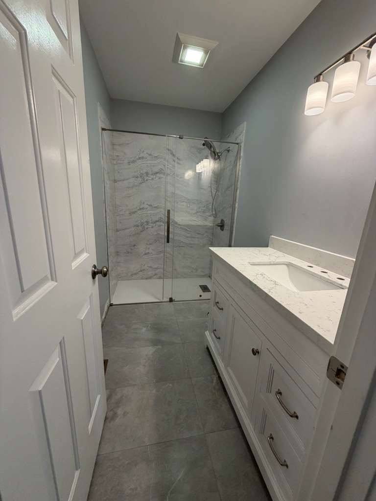 A clean, modern bathroom with a white vanity, marble-patterned countertop, and glass-enclosed shower.